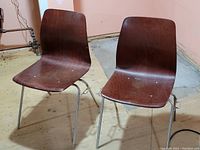 Pair of mid-century modern chairs with chrome legs and wooden molded seats showing wear.