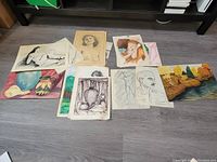Wide view of all artworks laid on floor, various pencil drawings and colorful paintings