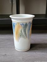 Front view showing white glazed ceramic wine cooler with abstract brushstroke design in blue, yellow, green