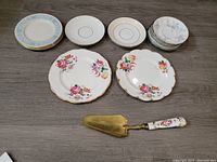 Photo of all 15 pieces, including Royal Albert salad plates, Paragon saucers, Royal Doulton plates, Lenox saucers, and the antique cake/pie lifter with floral handle and brass blade.