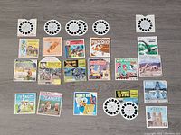 View-Master reels and accompanying booklets/sleeves arranged flat showing titles like Pinocchio, Donald Duck, Pendleton Round-Up, Peanuts, Dinosaurs, Jack and the Beanstalk, and others.