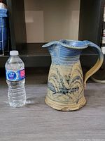 Side view of the large pottery jug next to a water bottle for size reference showing its height and shape.