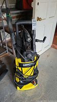 Front view of a yellow and black Karcher pressure washer with hose coiled around and spray gun attached.