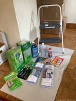 Full arrangement of cleaning supplies and step stool on white surface and hardwood floor