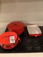 Three enameled cast iron cookware pieces (two round lidded pots and one rectangular pan) displayed on a stovetop