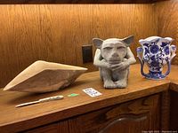Photo of three items: a maple wood bowl, moose antler utensil, and cement gargoyle figurine, on a wooden surface against a wood panel background.