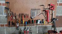 Photo of hand tools including wrenches, screwdrivers, and pliers hung on a pegboard above a concrete and brick wall.