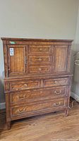 Front view of solid wood tall boy dresser showing three large drawers below and upper cabinet with three middle drawers flanked by two doors.