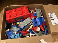 Box filled with assorted Lego pieces including large red Lego clock and various plates and bricks in different colors.
