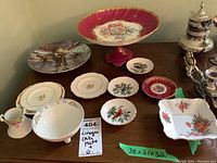 Overall view of a large Limoges footed cake plate in pink with floral center, surrounded by multiple smaller plates and decorative dishes featuring floral and bird designs. Includes Nippon and Royal Stafford items.