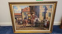 Full front view of framed painting showing village scene with riders, fountain, and woman