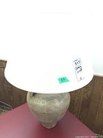 Pottery lamp with large fabric shade on a red surface against wood panel wall.