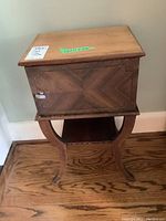 Front view of wood side table showing the compartment door with decorative wood grain pattern and curved legs.