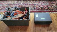 View of green plastic bin containing various extension cords and power bars in orange, blue, and white colors.