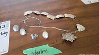 Photo showing the sterling silver bracelet, necklace with triangular pendant, floral brooch, set of stud earrings and two mismatched earrings laid out on a wooden surface.