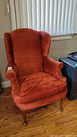 Wing back chair upholstered in reddish-brown crushed velvet fabric, shown from front left angle with wooden legs visible.