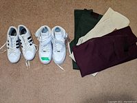 Photo showing Adidas white low-top sneakers and Nike Air Force 1 white high-top sneakers side by side, along with three pairs of folded skinny pants in green, off-white, and purple colors