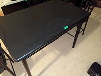 Black rectangular table showing tabletop wear and corner damage, with metal frame and legs.