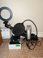 Ring light, pop filter, Samson microphone, tripod and cables in white box on carpet against wall