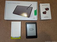 Photo showing boxed Star 05 V2 wireless tablet, Monster 100 AirLinks earbuds box, LG G5 smartphone box, and a powered on Amazon Kindle with battery low symbol.