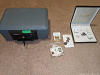 Photo showing the gray SentrySafe 1120 with key alongside jewelry, stamps, and medal items on carpet.