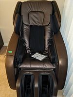 Front view of brown truMedic MC-2000 massage chair showing headrest, seat, footrest and user manual on seat