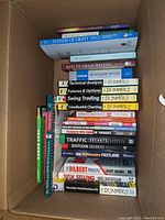 Photo of stacked books in box showing various titles primarily about business, investing, trading, writing, and self-help.