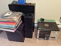 Photo showing stacked vinyl records, subwoofer speaker, and multiple black speakers together