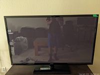 Front view of Samsung plasma TV powered off on stand with remote in front.