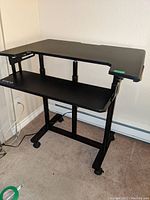 Front side view of black VIVO adjustable stand-up desk showing upper and lower platforms with caster wheels on base.