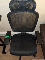 Front view of the Staples Hyken Technical Mesh Task Chair showing the black breathable mesh seat, cushioned armrests with green tape on left, and adjustable headrest.