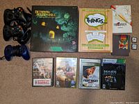 Lot overview photo showing controllers, board games, video game cases, cartridges, and art book.
