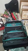 Photo showing Lucas branded green and black travel bag with multiple compartments in open state, floral handbag and other small wallets in background
