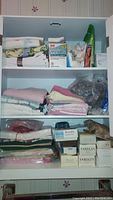 Full view of cabinet shelves showing folded towels, box of CVS Epsom salts, and multiple boxed soap bars.