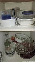 Overview of various casserole dishes, glass bowls, juicer, chopper, and ramekins arranged inside shelves.