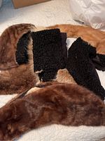 Seven fur collars laid out on a bed. Five appear unique and two are identical black curly fur collars. Collars show signs of wear and dirt.