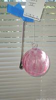Photo of two glass hanging pieces, one spherical ball with pink swirls and one elongated teardrop-shaped piece with pink swirls.