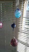 Three hanging glass balls of different shapes and colors against window blinds.