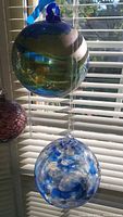 Two decorative glass balls hanging in front of blinds, showing their colors and swirl patterns