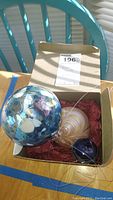 Box containing three glass balls including large blue ball with colorful ribbons, medium cream swirled ball, and small dark blue ball.
