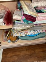 Shelf with assorted cloth napkins and placemats, some in plastic wrapping, in varied colors and patterns including florals.