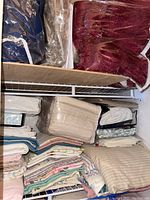 View of folded linens including blankets and pillowcases arranged on shelves and stacked.