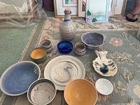 Overview of multiple pottery items including carafe, cups, bowls, plates, and dish with floral design on carpet