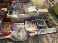 Overall view of the stationery collection showing plastic bins containing cards, envelopes, note pads, and pens laid out on carpet floor.