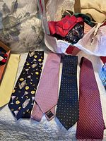 Five men's ties laid out flat, showing front designs and colors including yellow-striped, cocktail-themed navy, pink geometric, dark blue polka dots, and red patterned.