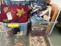 Two plastic totes packed with assorted linens, placemats, napkins, and holiday decor items.