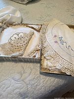 Doilies arranged in boxes and spread on quilted bedspread showing variety of lace and fabric types.