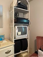 Full view of the white wicker 5 tier bookcase with shelves showing stacked electronic components and vintage TV (not included in lot).