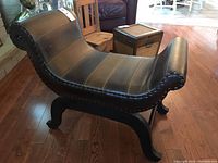 Side angle showing curved leather seat with nailhead trim and wood veneer base with curved legs
