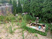 Overview of brick patio corner with multiple garden ornaments including fountain basin, planter, statuettes and foliage